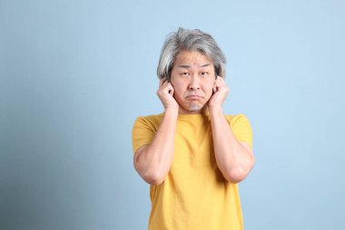 The senior Asian man with yellow t shirt standing on the blue background.