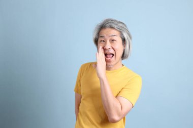The senior Asian man with yellow t shirt standing on the blue background.
