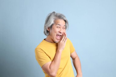 The senior Asian man with yellow t shirt standing on the blue background.