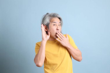 The senior Asian man with yellow t shirt standing on the blue background.