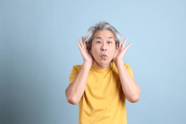 The senior Asian man with yellow t shirt standing on the blue background.