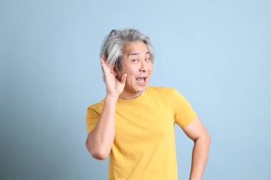 The senior Asian man with yellow t shirt standing on the blue background.