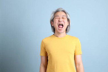 The senior Asian man with yellow t shirt standing on the blue background.