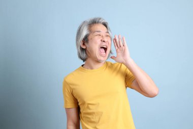 The senior Asian man with yellow t shirt standing on the blue background.