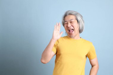 The senior Asian man with yellow t shirt standing on the blue background.
