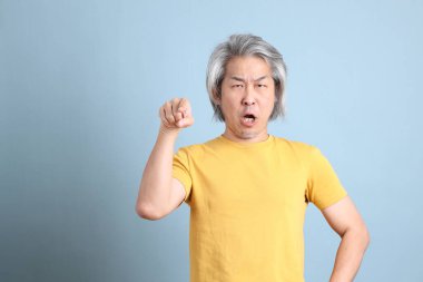 The senior Asian man with yellow t shirt standing on the blue background.