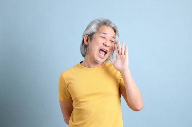 The senior Asian man with yellow t shirt standing on the blue background.