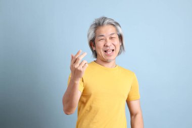 The senior Asian man with yellow t shirt standing on the blue background.
