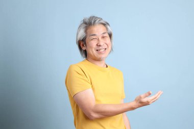 The senior Asian man with yellow t shirt standing on the blue background.