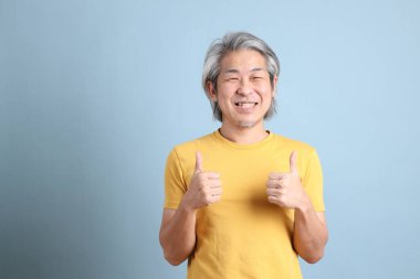 The senior Asian man with yellow t shirt standing on the blue background.