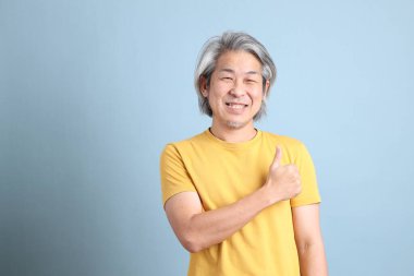 The senior Asian man with yellow t shirt standing on the blue background.