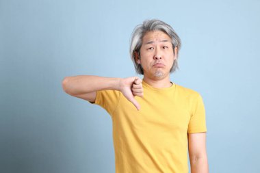 The senior Asian man with yellow t shirt standing on the blue background.