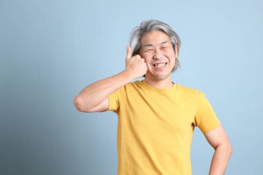 The senior Asian man with yellow t shirt standing on the blue background.