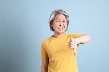 The senior Asian man with yellow t shirt standing on the blue background.