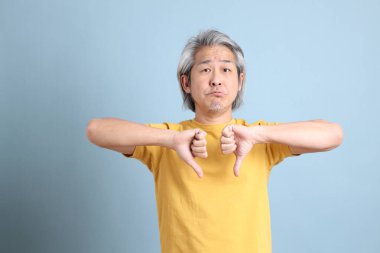 The senior Asian man with yellow t shirt standing on the blue background.