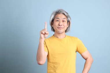The senior Asian man with yellow t shirt standing on the blue background.