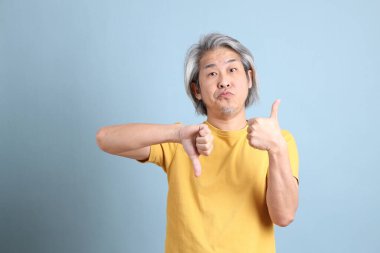 The senior Asian man with yellow t shirt standing on the blue background.