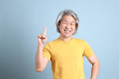 The senior Asian man with yellow t shirt standing on the blue background.