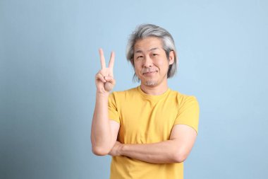 The senior Asian man with yellow t shirt standing on the blue background.