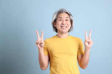 The senior Asian man with yellow t shirt standing on the blue background.