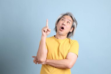 The senior Asian man with yellow t shirt standing on the blue background.
