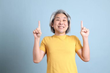 The senior Asian man with yellow t shirt standing on the blue background.