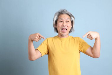The senior Asian man with yellow t shirt standing on the blue background.