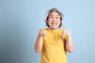 The senior Asian man with yellow t shirt standing on the blue background.
