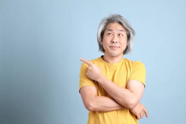 The senior Asian man with yellow t shirt standing on the blue background.