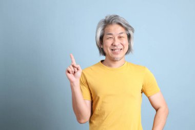 The senior Asian man with yellow t shirt standing on the blue background.