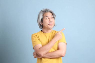 The senior Asian man with yellow t shirt standing on the blue background.