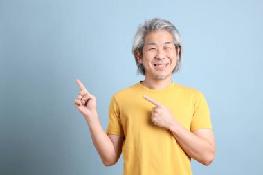The senior Asian man with yellow t shirt standing on the blue background.