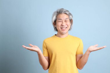 The senior Asian man with yellow t shirt standing on the blue background.
