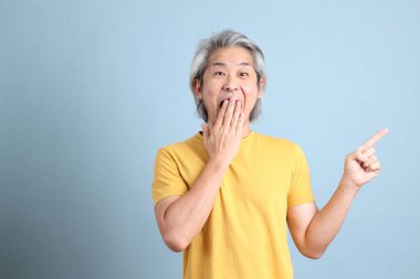 The senior Asian man with yellow t shirt standing on the blue background.