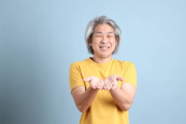 The senior Asian man with yellow t shirt standing on the blue background.