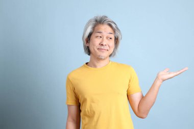 The senior Asian man with yellow t shirt standing on the blue background.