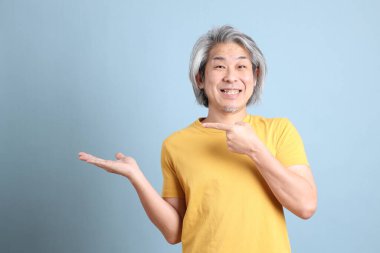 The senior Asian man with yellow t shirt standing on the blue background.