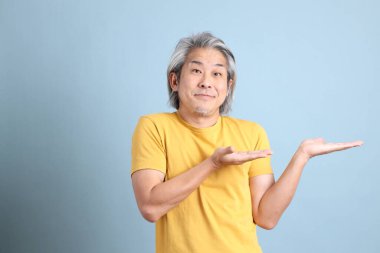 The senior Asian man with yellow t shirt standing on the blue background.