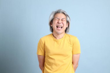 The senior Asian man with yellow t shirt standing on the blue background.