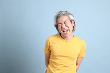 The senior Asian man with yellow t shirt standing on the blue background.