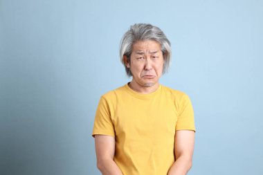 The senior Asian man with yellow t shirt standing on the blue background.