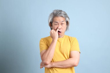 The senior Asian man with yellow t shirt standing on the blue background.