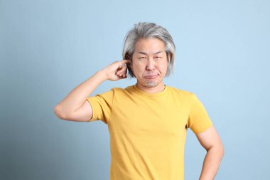 The senior Asian man with yellow t shirt standing on the blue background.