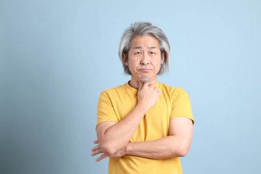 The senior Asian man with yellow t shirt standing on the blue background.