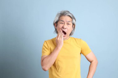 The senior Asian man with yellow t shirt standing on the blue background.