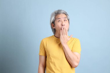 The senior Asian man with yellow t shirt standing on the blue background.