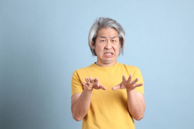 The senior Asian man with yellow t shirt standing on the blue background.