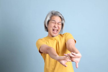 The senior Asian man with yellow t shirt standing on the blue background.