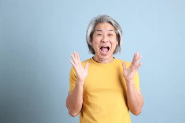 The senior Asian man with yellow t shirt standing on the blue background.