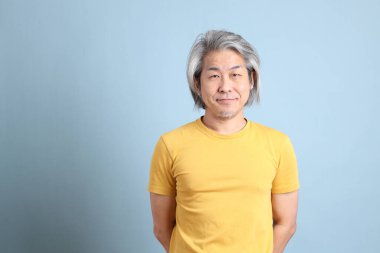 The senior Asian man with yellow t shirt standing on the blue background.